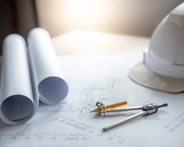 Compass tool and safety helmet on architectural drawing plan of house project, blueprint rolls on working table, Architecture and building construction industry concepts